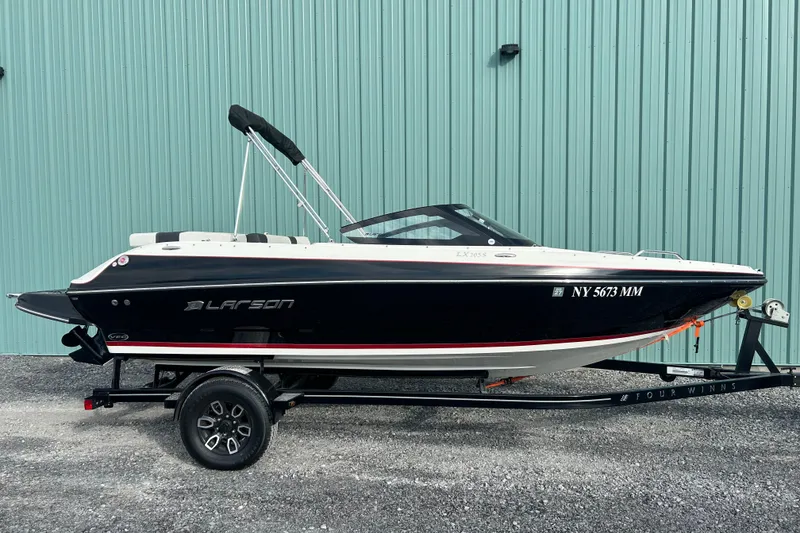 Slide: The Image of 2016 Larson LX 205S IO boat on trailer, parked by a teal wall. - 7