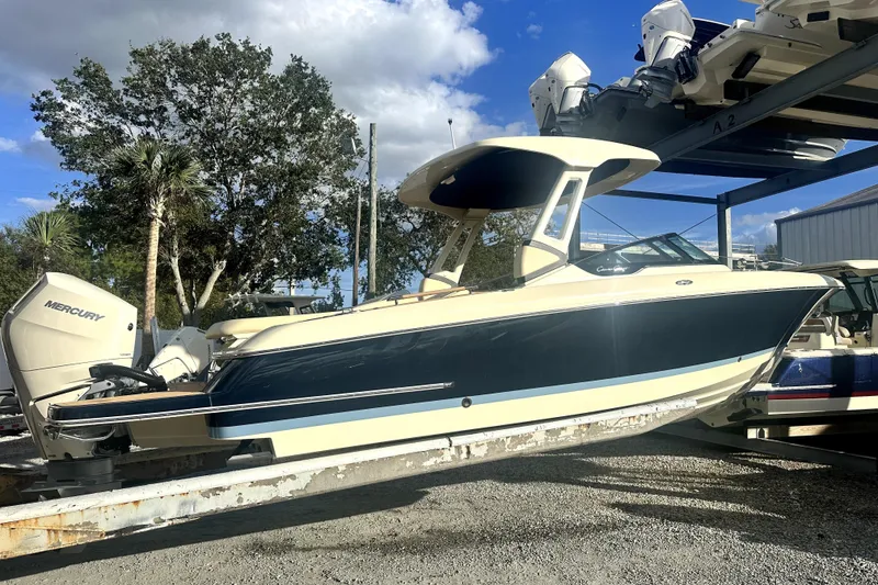 Slide: The Image of 2026 Chris-Craft Sportster 28 boat with Mercury engine on a lift, under a blue sky. - 2