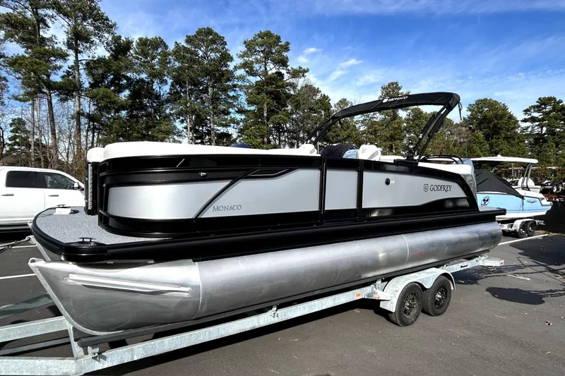 The Image of 2026 Godfrey Monaco 235 ULC pontoon boat on trailer, parked outdoors. - 0