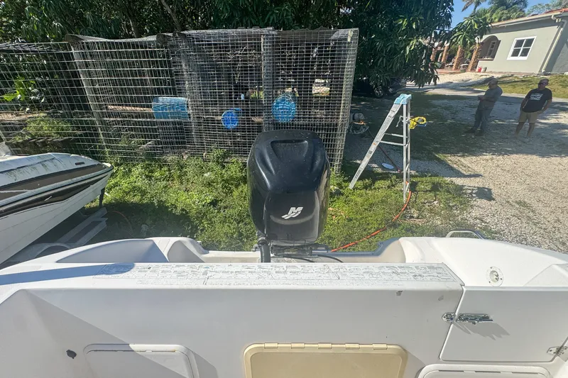 Slide: The Image of 2005 Pro-Line 24 Sport boat with outboard motor, parked near a fenced area. - 57