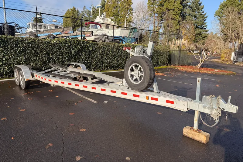 Slide: The Image of Boat trailer parked on asphalt, surrounded by trees and boats in the background. - 51