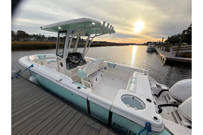 The Image of 2025 Robalo R250 Center Console boat on calm water, near a wooded shoreline. - 0