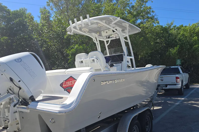 Slide: The Image of 2018 Sportsman Heritage 241 Center Console boat on trailer, parked near trees. - 8