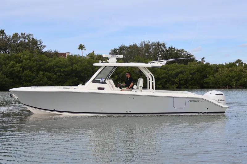 Slide: The Image of 2021 Pursuit S 328 Sport boat cruising on calm water near lush greenery. - 2