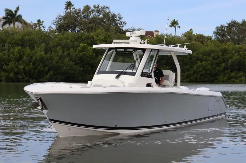 Slide: The Image of 2021 Pursuit S 328 Sport boat cruising on calm water near lush greenery. - 4