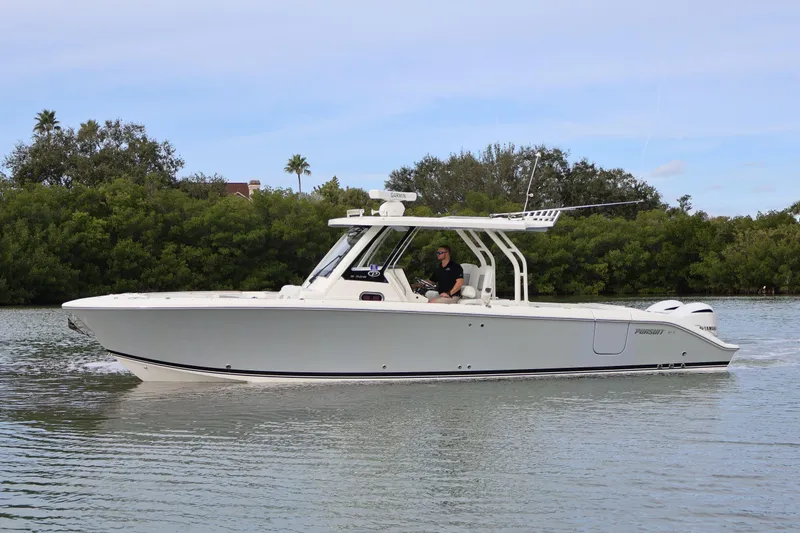 Slide: The Image of 2021 Pursuit S 328 Sport boat cruising on calm water near lush greenery. - 8