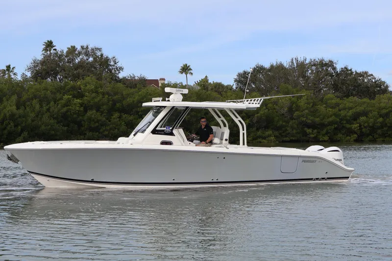 Slide: The Image of 2021 Pursuit S 328 Sport boat cruising on calm water near lush greenery. - 9