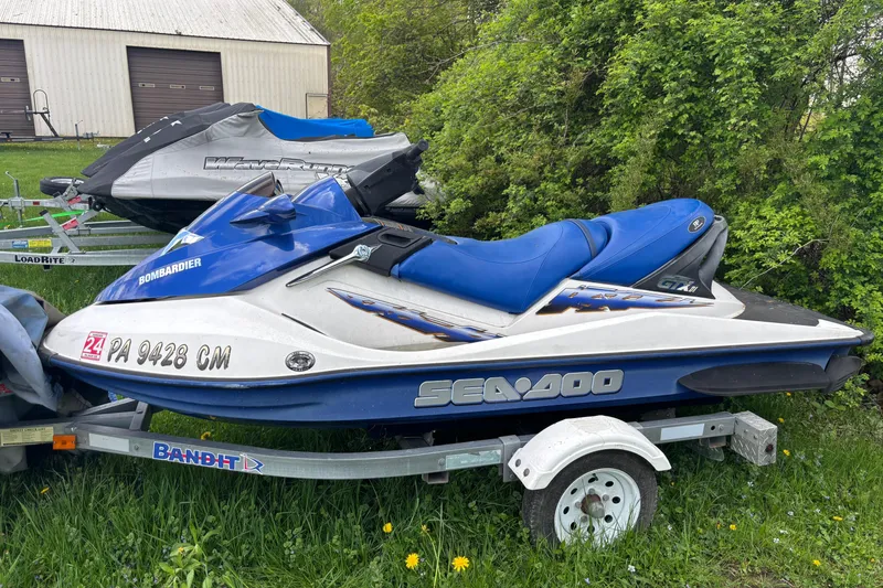 The Image of 2002 Sea-Doo GTX DI jet ski on trailer, parked on grass near a building. - 1