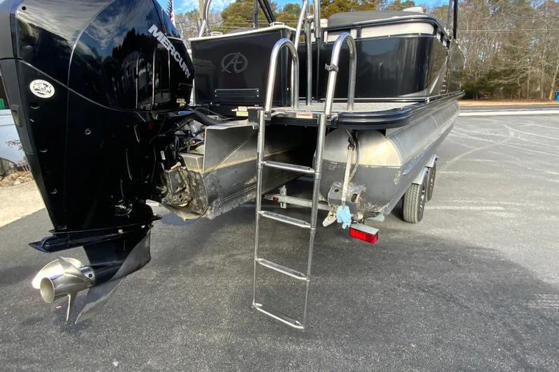 Slide: The Image of 2021 Avalon LSZ Quad Lounger boat with Mercury outboard motor and ladder, parked on pavement. - 11