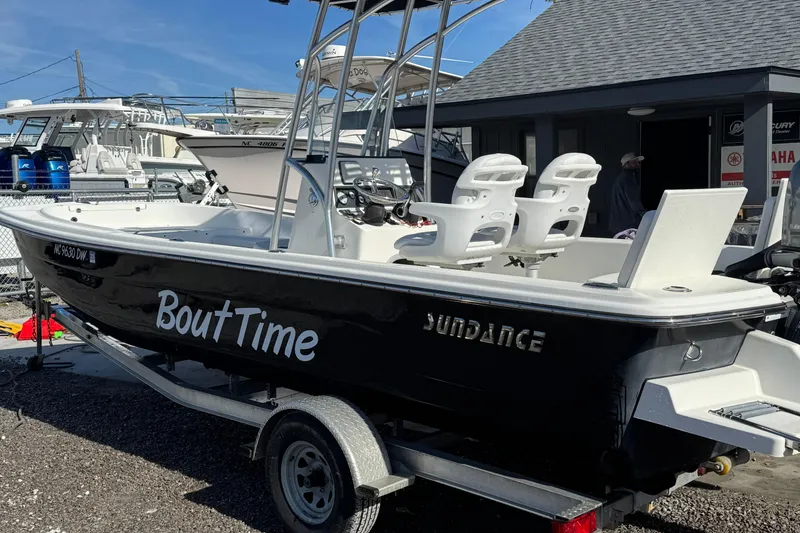 Slide: The Image of 2013 Sundance DX22 boat named "Bout Time" on trailer, docked near other boats. - 2