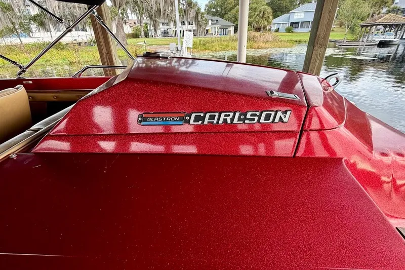 Slide: The Image of 1981 Glastron Carlson C-512 boat in vibrant red, docked by a serene lakeside. - 7
