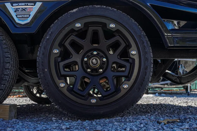 Slide: The Image of Black wheel of 2021 Skeeter FXR20 Apex boat trailer on gravel surface. - 19