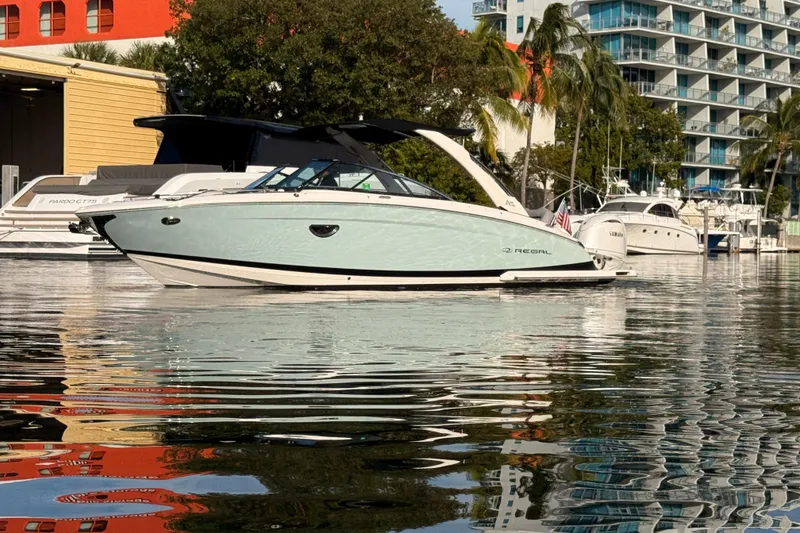 The Image of 2024 Regal LX9 boat docked in a marina, surrounded by modern buildings and palm trees. - 0