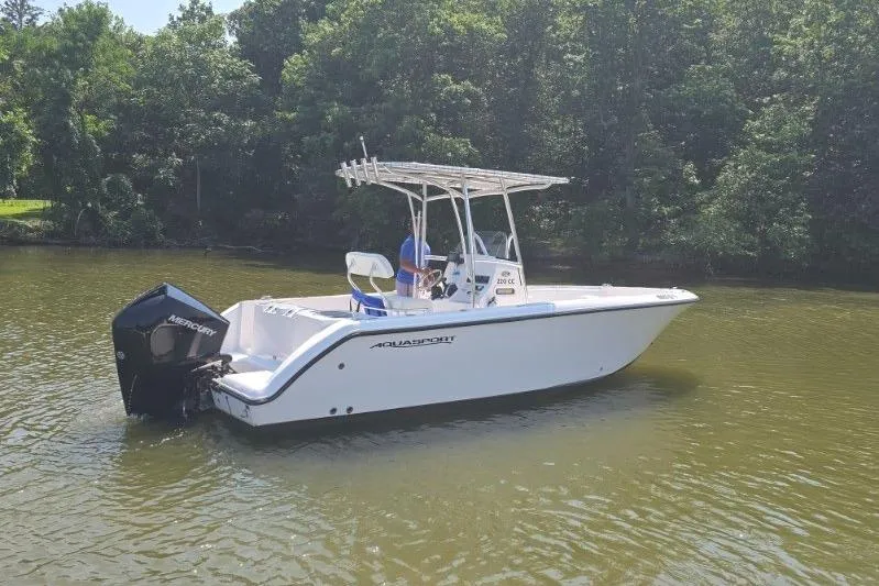 The Image of 2024 Aquasport 2200 Center Console boat on calm water, surrounded by trees. - 1