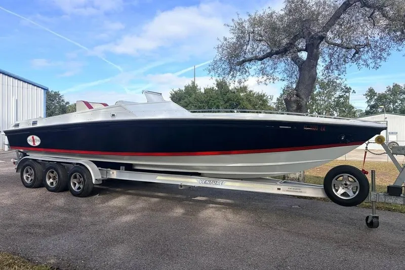 The Image of 1983 Cigarette 24' Classic boat on trailer, parked outdoors near trees and buildings. - 0