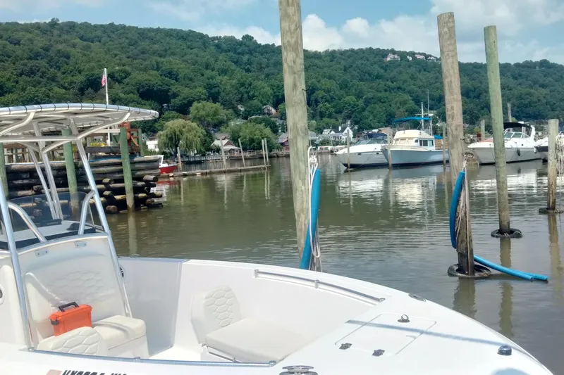 Slide: The Image of 2024 Aquasport 2200 Center Console boat docked in a scenic marina setting. - 2