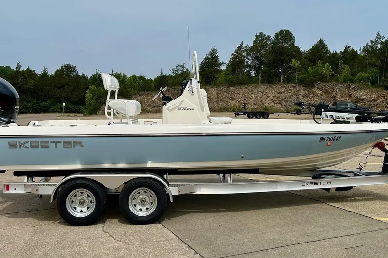 Slide: The Image of 2023 Skeeter SX210 boat on trailer, parked outdoors with trees in background. - 20