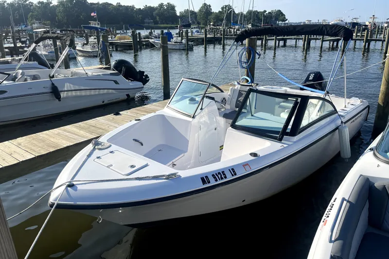 Slide: The Image of 2024 Aquasport 2200 Dual Console boat docked at a marina, surrounded by other vessels. - 2