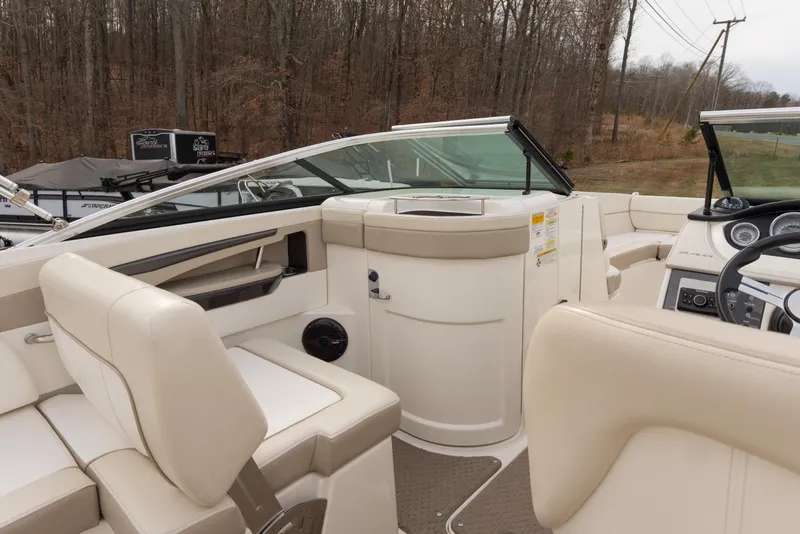 Slide: The Image of 2014 Sea Ray 240 Sundeck Outboard interior with beige seating and dashboard, surrounded by trees. - 15