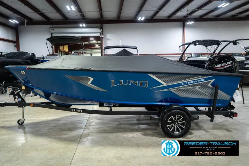 Slide: The Image of 2026 Lund 1675 Adventure SS boat in showroom, blue with cover, on trailer. - 52