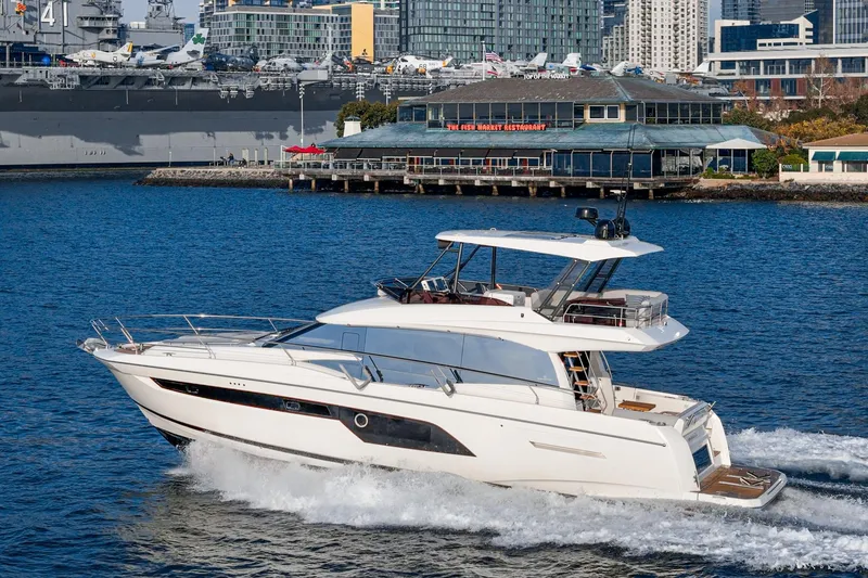 Slide: The Image of 2023 Prestige 520 yacht cruising near urban waterfront with naval ship in background. - 10