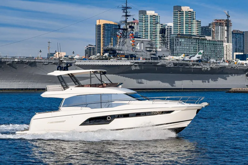 Slide: The Image of 2023 Prestige 520 yacht cruising near a large battleship with city skyline backdrop. - 15
