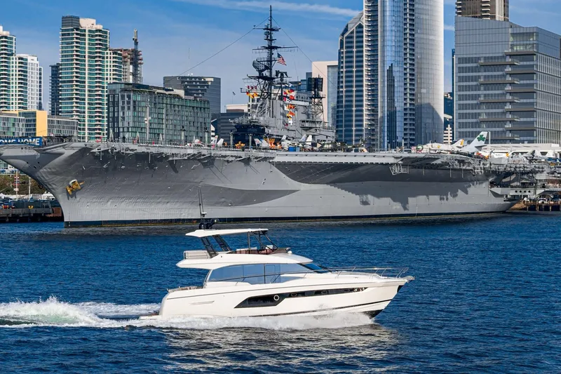 Slide: The Image of 2023 Prestige 520 yacht cruising near a large battleship in an urban harbor setting. - 25
