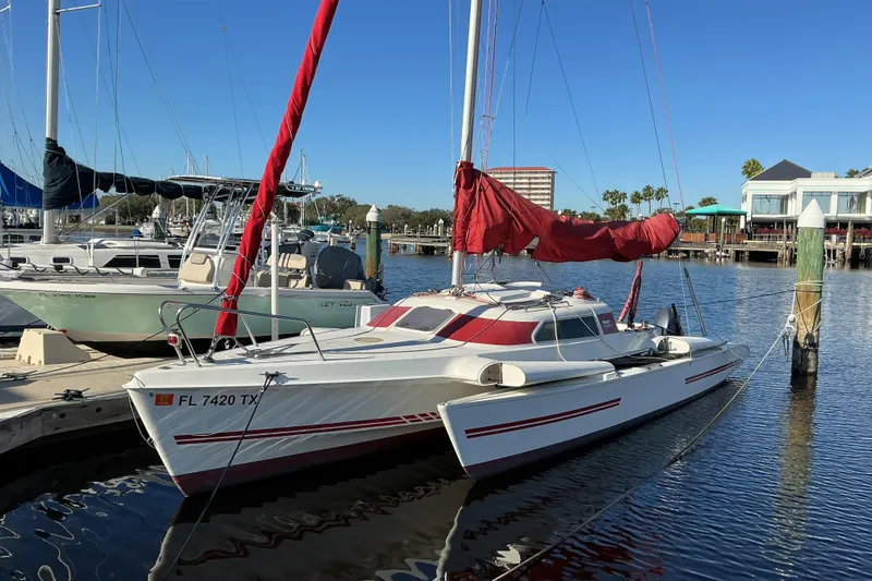 The Image of 1992 Dragonfly 800 Swing Wing sailboat docked in marina, red sail, clear sky. - 0