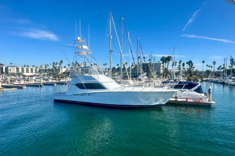 The Image of 2000 Hatteras 60 Convertible yacht docked in a sunny marina with clear blue skies. - 0