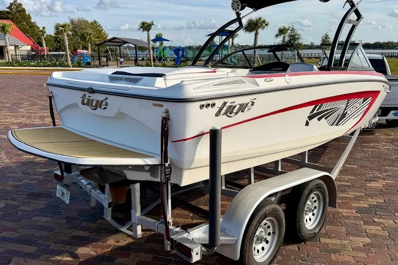 Slide: The Image of 2012 Tigé R20 boat on trailer, parked near waterfront with palm trees. - 2
