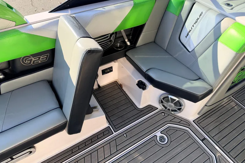 Slide: The Image of 2014 Nautique Super Air Nautique G23 interior with green and gray seating, speaker, and flooring. - 17