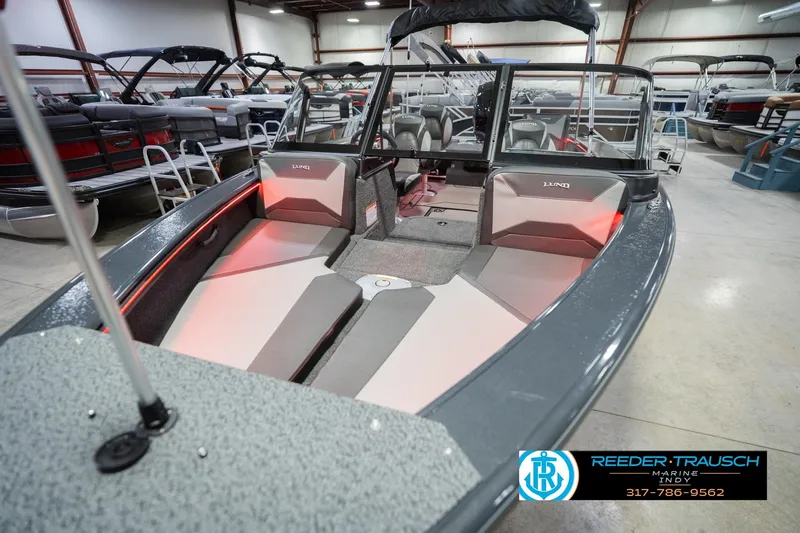 Slide: The Image of 2026 Lund 1875 Crossover XS boat interior in a showroom, featuring seating and storage. - 12