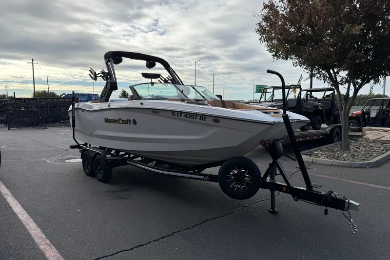 Slide: The Image of 2025 MasterCraft X24 boat on trailer in parking lot, overcast sky. - 18