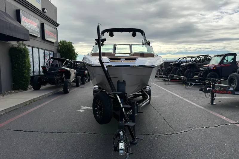 Slide: The Image of 2025 MasterCraft X24 boat on trailer in dealership lot with off-road vehicles. - 19