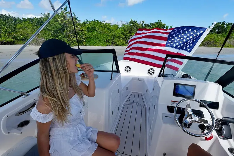 Slide: The Image of Manufacturer Provided Image: Woman enjoying a snack on a 2025 Aquasport 22AS Dual Console boat with American flag. - 4