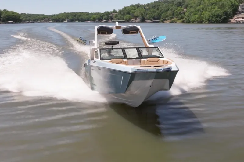 Slide: The Image of 2025 MasterCraft XStar 25 boat cruising on a scenic lake with lush green surroundings. - 7
