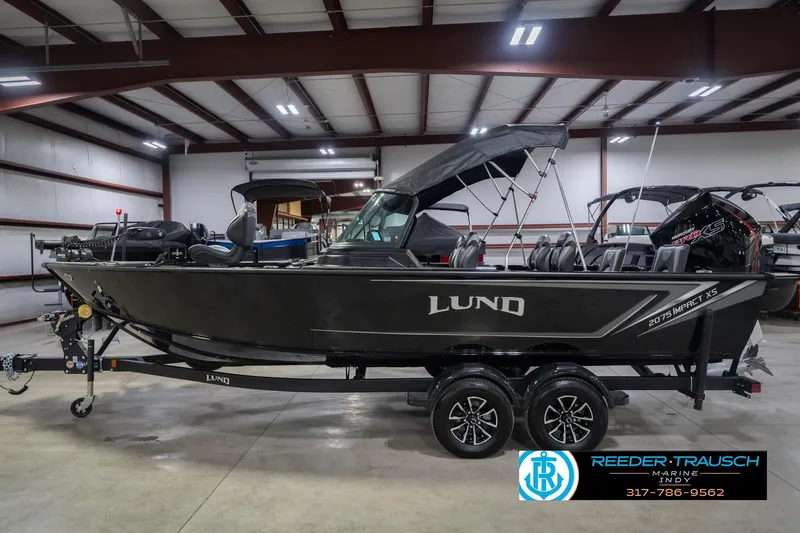 Slide: The Image of 2026 Lund 2075 Impact XS boat in showroom, side view with trailer and canopy. - 11