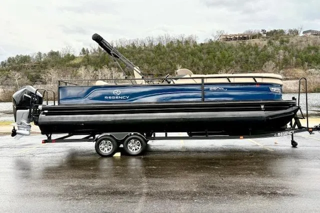 Slide: The Image of 2025 Regency 250 DL3 pontoon boat on trailer, parked near a scenic river. - 1