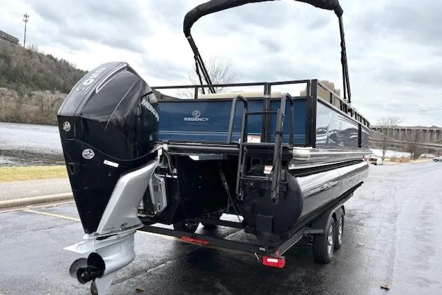 Slide: The Image of 2025 Regency 250 DL3 pontoon boat on trailer, parked near a river. - 10