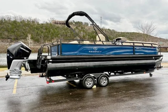 Slide: The Image of 2025 Regency 250 DL3 pontoon boat on trailer, parked outdoors, with Mercury outboard motor. - 4