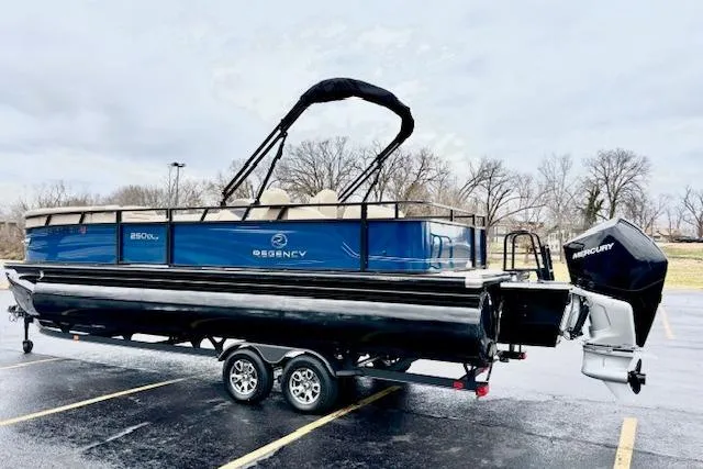 Slide: The Image of 2025 Regency 250 DL3 pontoon boat on trailer, parked in a lot, overcast sky. - 5