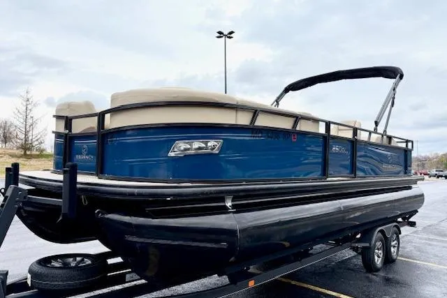 Slide: The Image of 2025 Regency 250 DL3 pontoon boat on trailer, blue and beige design, parked outdoors. - 7