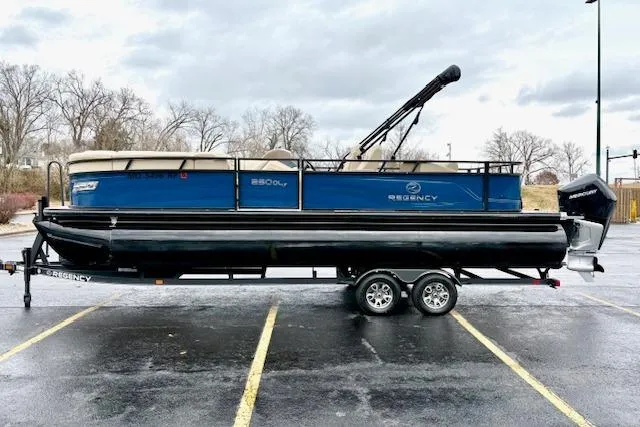 Slide: The Image of 2025 Regency 250 DL3 pontoon boat on trailer in parking lot, overcast sky. - 8
