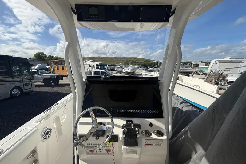 Slide: The Image of Edgewater 262CC 2021 boat dashboard with steering wheel and controls, parked in a marina. - 6