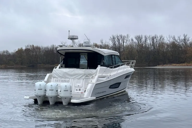 Slide: The Image of 2021 Regal 38 XO boat on calm water with wooded shoreline background. - 2