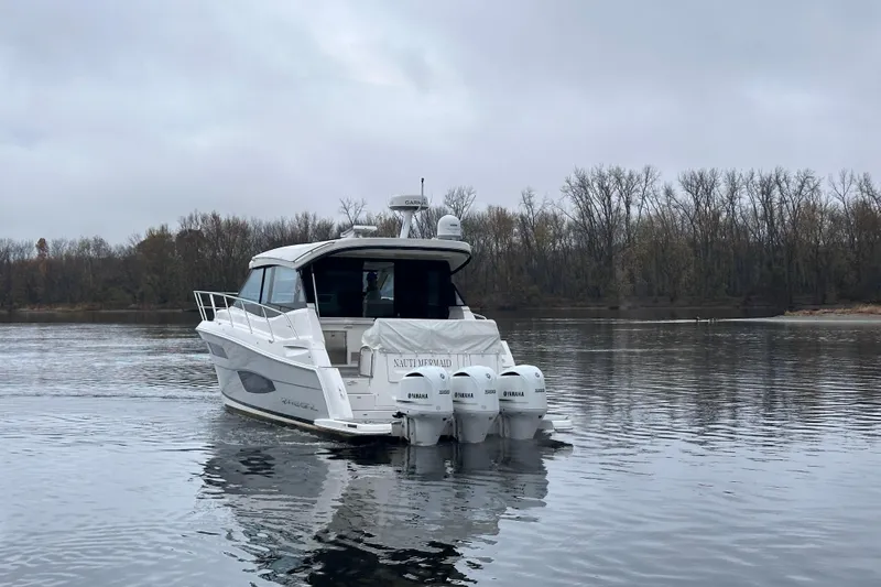 Slide: The Image of 2021 Regal 38 XO boat on calm water with overcast sky and wooded shoreline. - 4