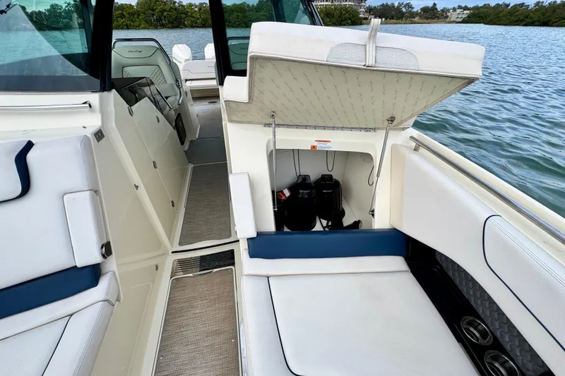 Slide: The Image of 2021 Chris-Craft Calypso 35 interior with open storage compartment, white seating, and scenic water view. - 45