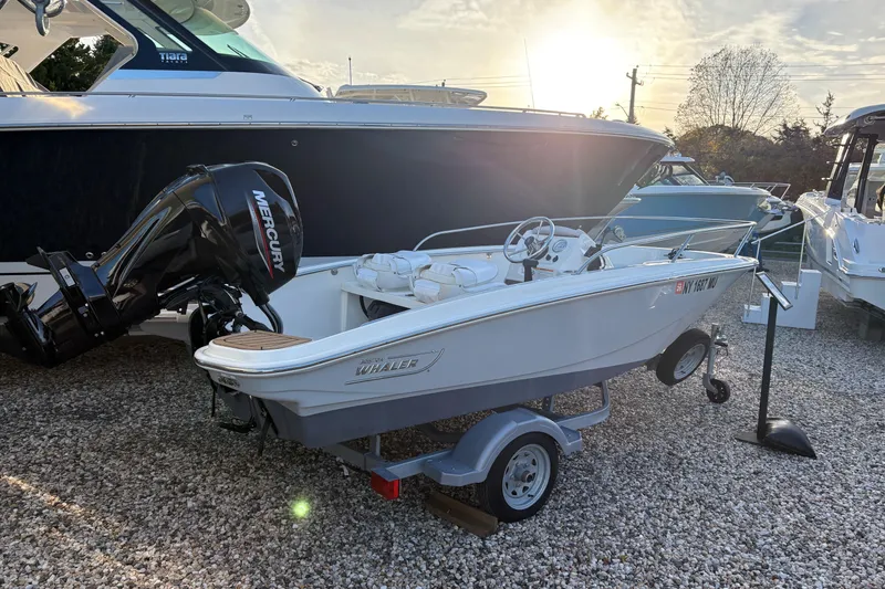 The Image of 2023 Boston Whaler 130 Super Sport boat on trailer, with Mercury engine, in a marina setting. - 0