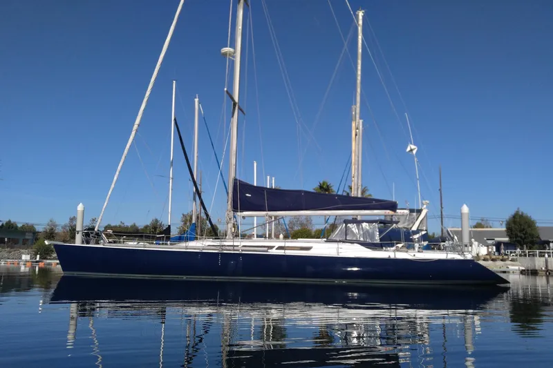 The Image of 1985 MacGregor 65 sailboat docked on calm water under clear blue sky. - 0