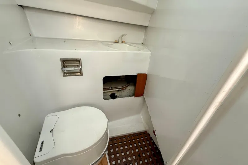 Slide: The Image of 1985 MacGregor 65 yacht bathroom with toilet, sink, and wooden floor grate. - 21